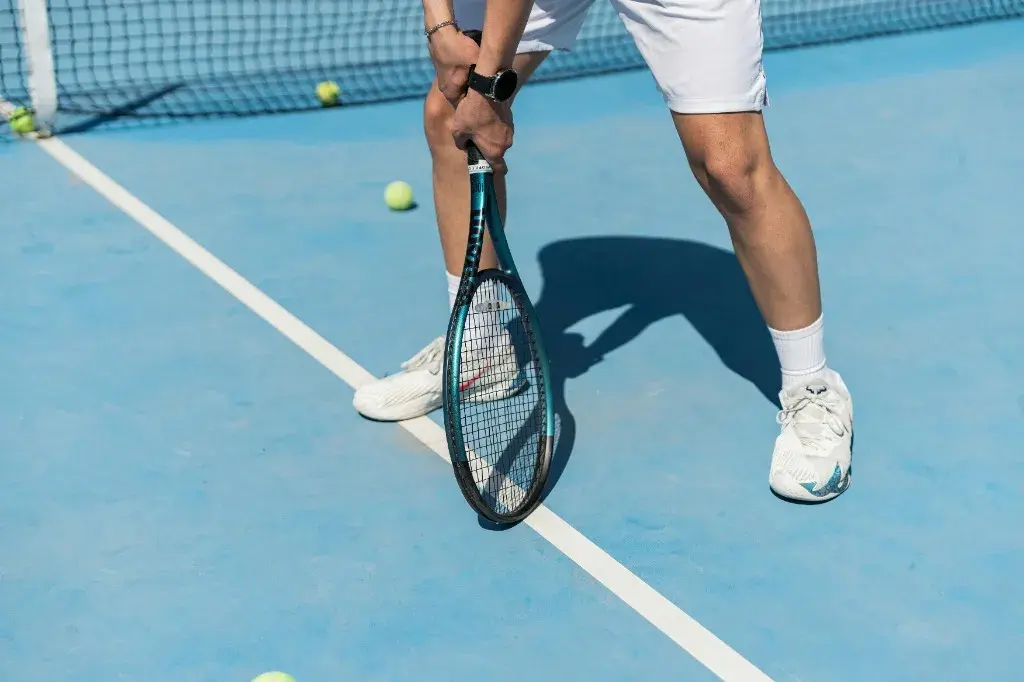 Wilson Pro Staff v14 tennis racket leaning against a net at sunset, highlighting the v14 paint finish and box beam design.